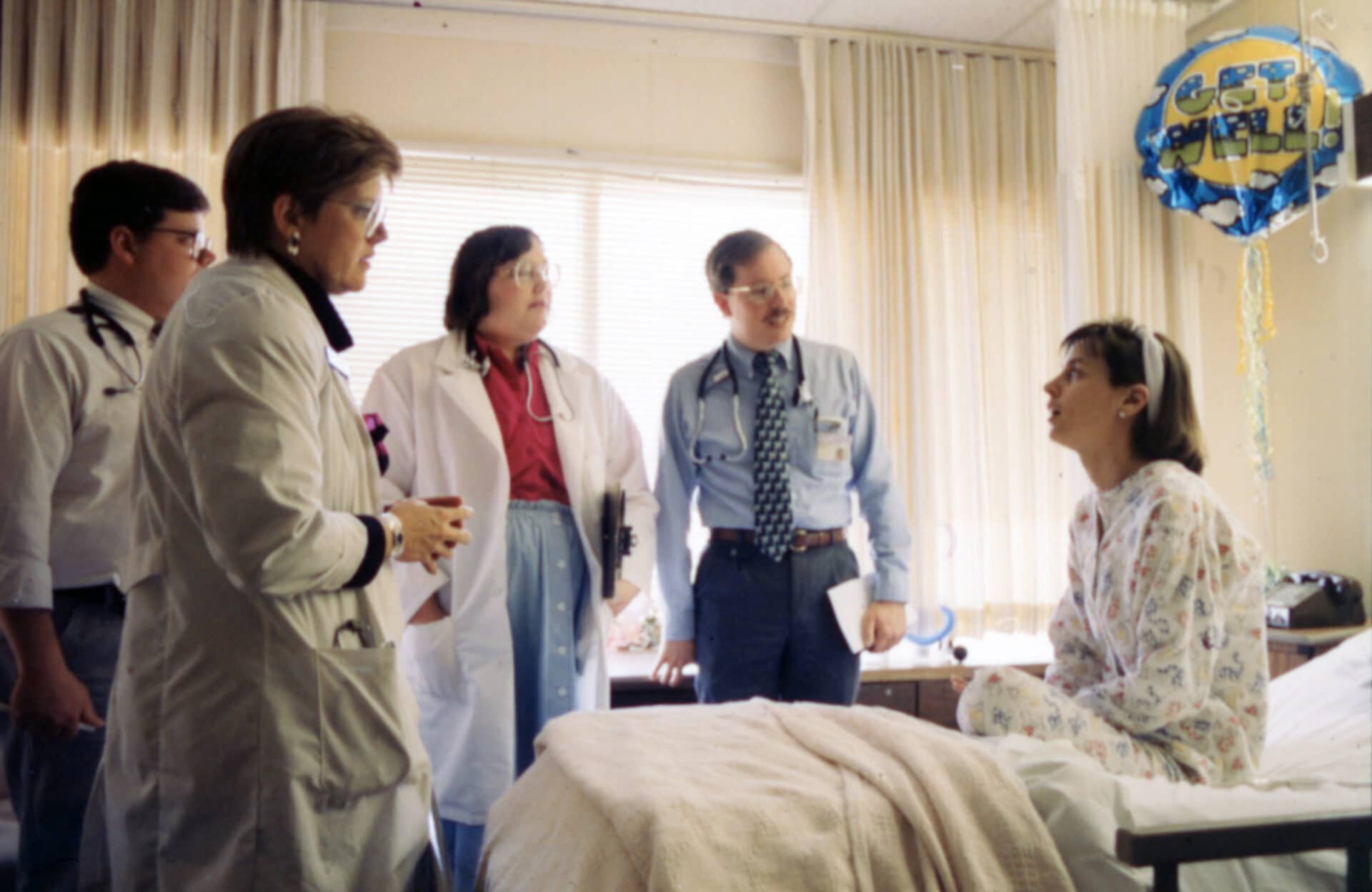 group of people interacting with a person sitting on a bed.