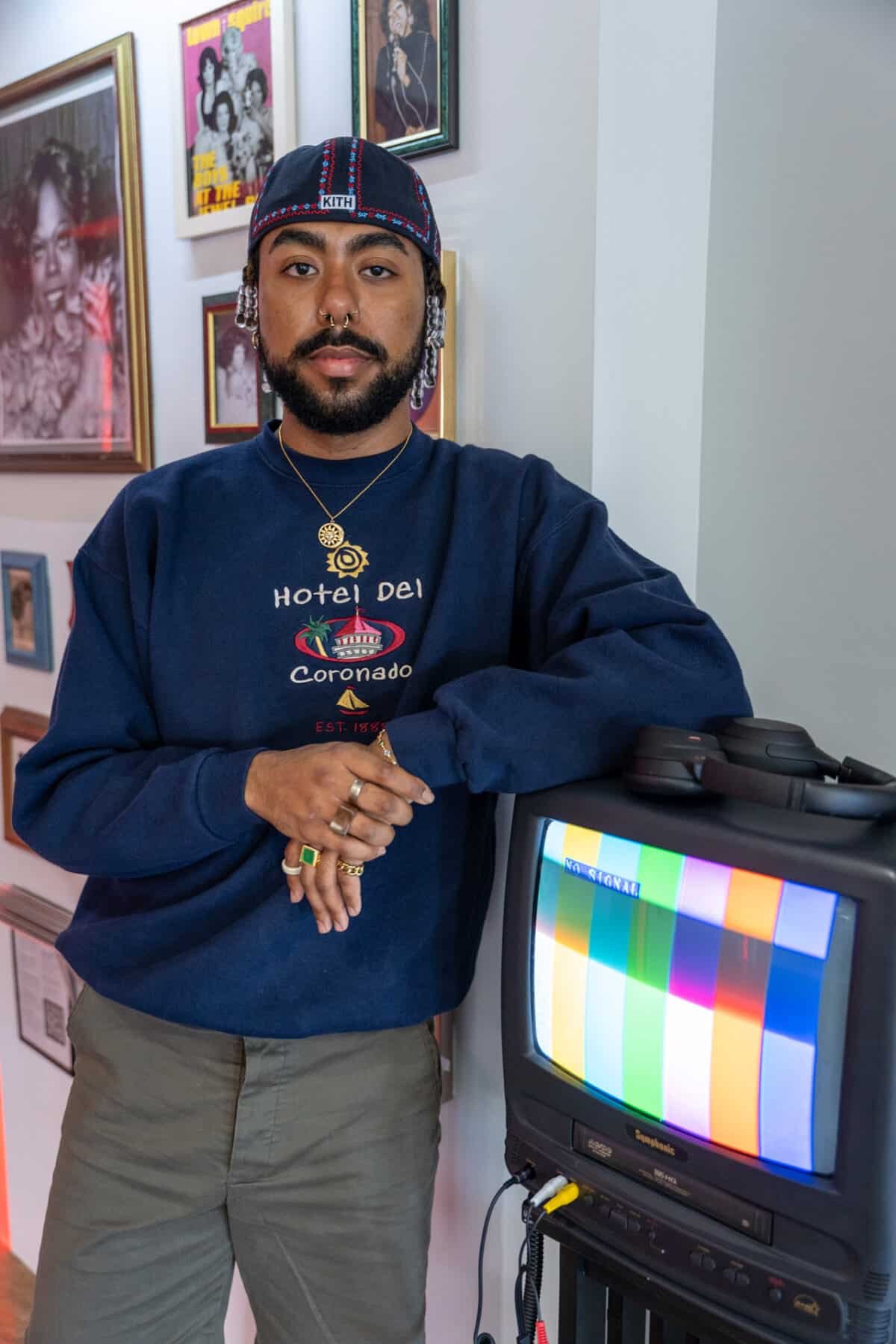 Nasir Anthony Montalvo leaning against a television with stripes of color on the screen that is part of the exhibit