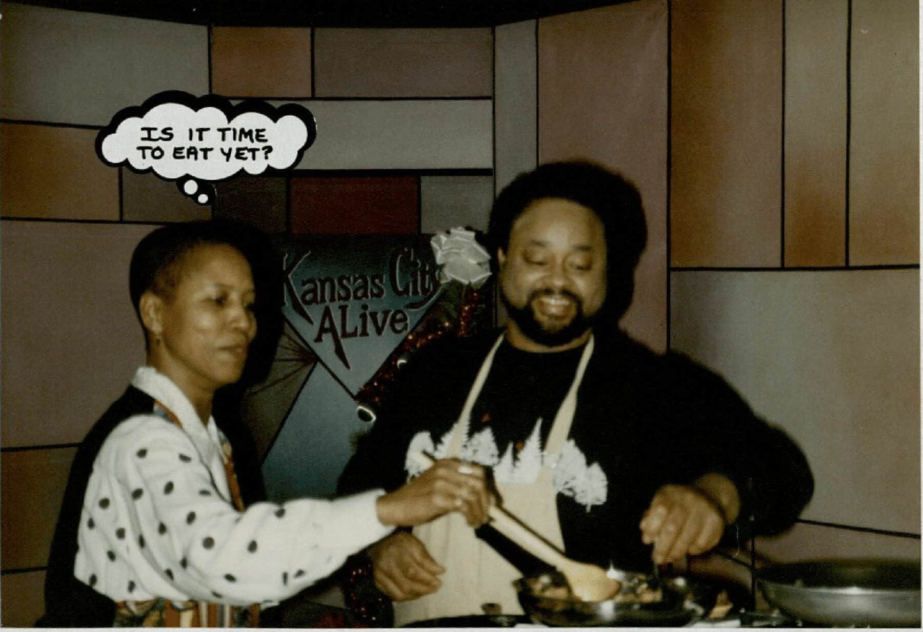 A photo of two people cooking, one with a thought bubble over their head that says "Is it time to eat yet?"